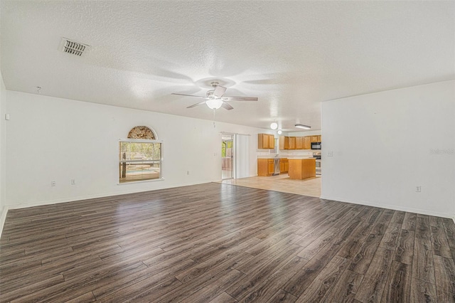 unfurnished living room featuring baseboards, visible vents, a ceiling fan, light wood-style flooring, and a textured ceiling