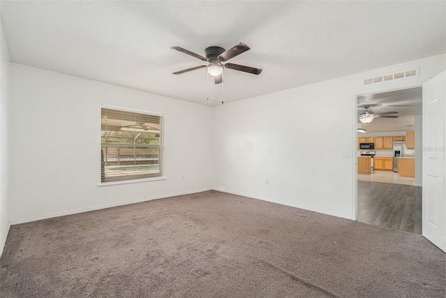 empty room with baseboards, visible vents, a ceiling fan, a textured ceiling, and carpet flooring