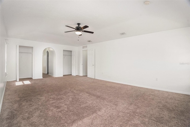 unfurnished bedroom with arched walkways, a textured ceiling, carpet flooring, and multiple closets