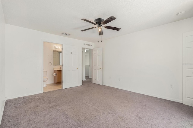 unfurnished bedroom featuring visible vents, connected bathroom, light carpet, and a textured ceiling