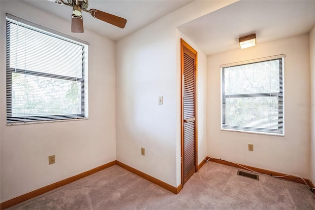 carpeted spare room with baseboards, ceiling fan, visible vents, and a healthy amount of sunlight