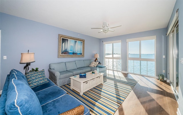 living area featuring a water view, a ceiling fan, baseboards, and wood finished floors