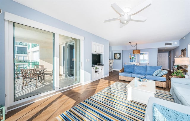 living area featuring baseboards, visible vents, ceiling fan, and wood finished floors