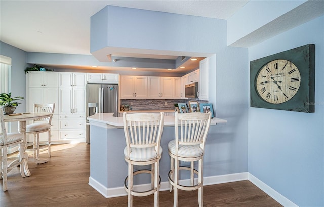 kitchen with tasteful backsplash, baseboards, dark wood-type flooring, a peninsula, and stainless steel appliances