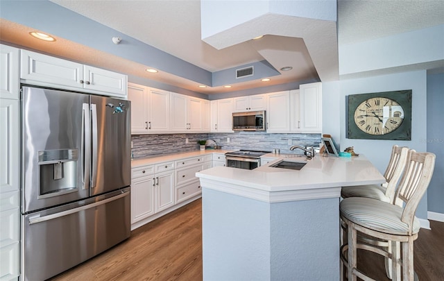 kitchen with a peninsula, wood finished floors, a sink, light countertops, and appliances with stainless steel finishes