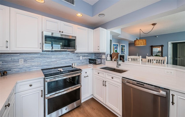 kitchen with decorative light fixtures, stainless steel appliances, light countertops, white cabinetry, and a sink