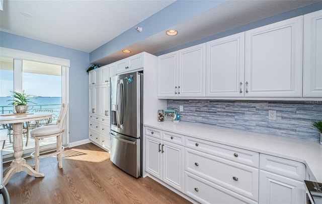 kitchen featuring white cabinetry, light countertops, stainless steel refrigerator with ice dispenser, backsplash, and light wood finished floors