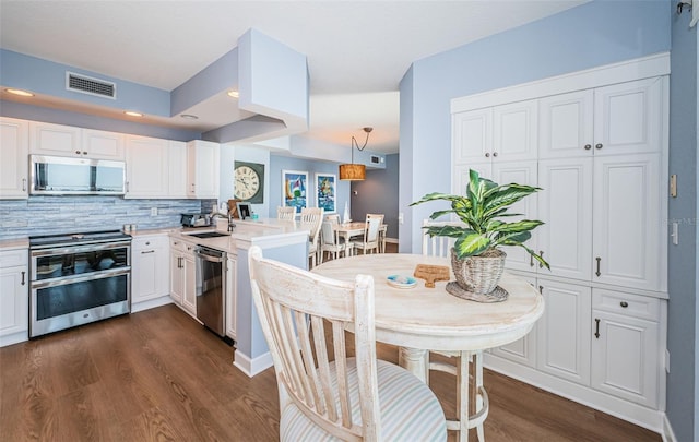 kitchen with a peninsula, dark wood-style flooring, visible vents, white cabinets, and appliances with stainless steel finishes