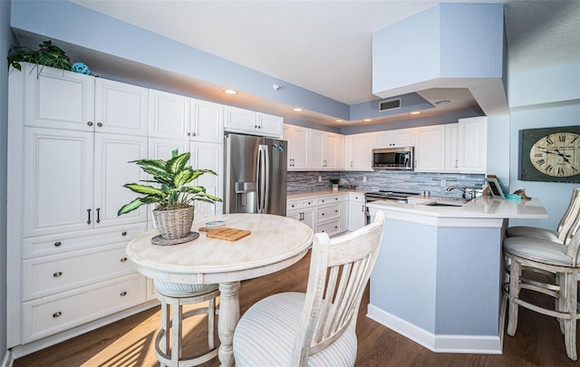 kitchen with visible vents, a peninsula, stainless steel appliances, white cabinetry, and a sink