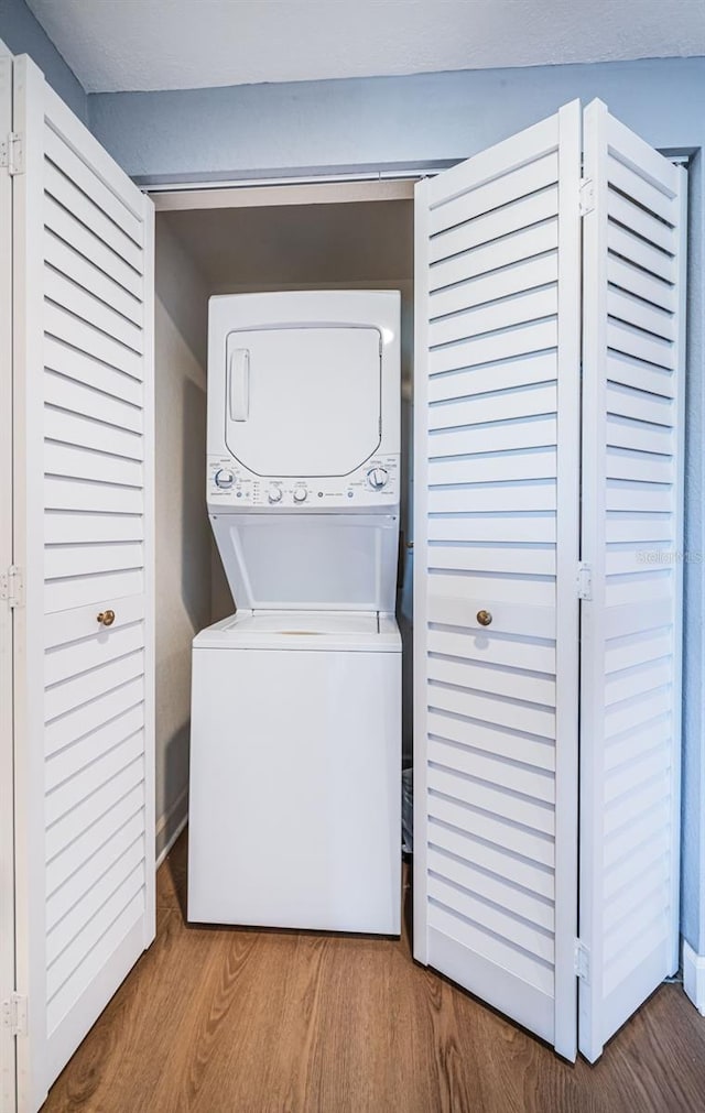 clothes washing area featuring laundry area, stacked washer / dryer, and wood finished floors