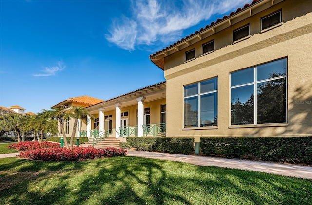 exterior space featuring a porch, a tiled roof, a front lawn, and stucco siding