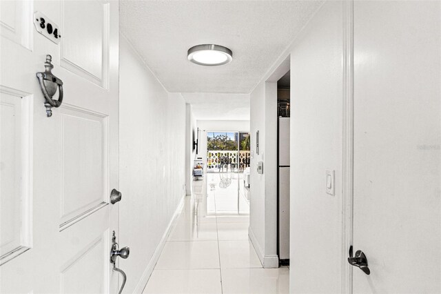 hall featuring baseboards, a textured ceiling, and light tile patterned flooring