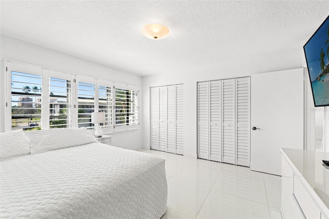 bedroom with a textured ceiling, multiple closets, and light tile patterned flooring