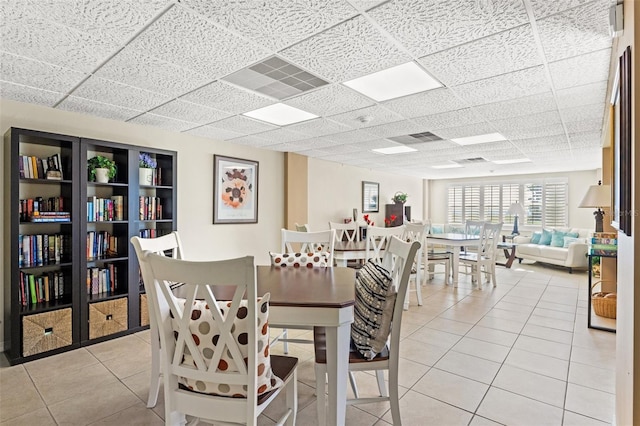 dining space featuring visible vents, a drop ceiling, and light tile patterned flooring