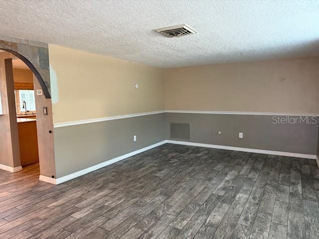 spare room with arched walkways, visible vents, and dark wood finished floors