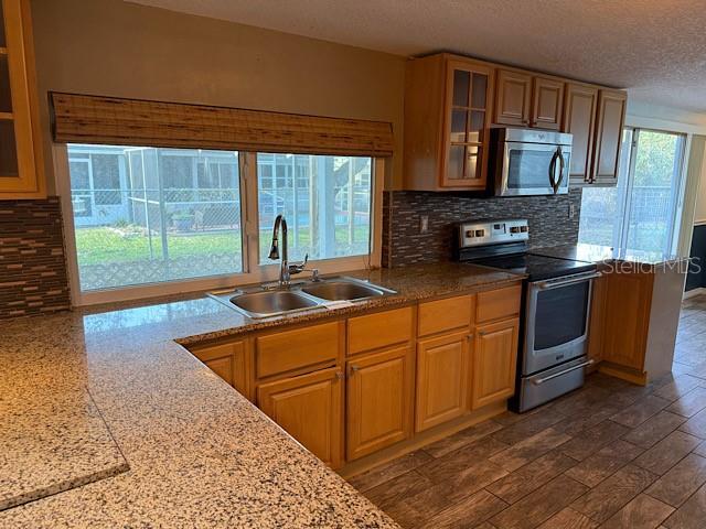 kitchen with stainless steel appliances, backsplash, glass insert cabinets, a sink, and light stone countertops