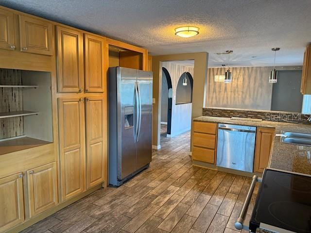 kitchen with wood finished floors, hanging light fixtures, stainless steel appliances, a textured ceiling, and a sink