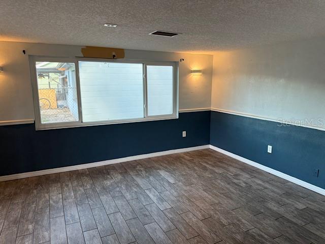 empty room with baseboards, visible vents, dark wood finished floors, and a textured ceiling