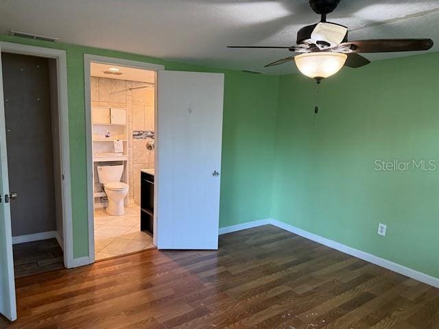 unfurnished bedroom with ensuite bath, dark wood-style floors, visible vents, and baseboards