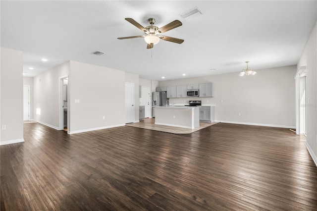 unfurnished living room featuring visible vents, dark wood finished floors, baseboards, and ceiling fan with notable chandelier