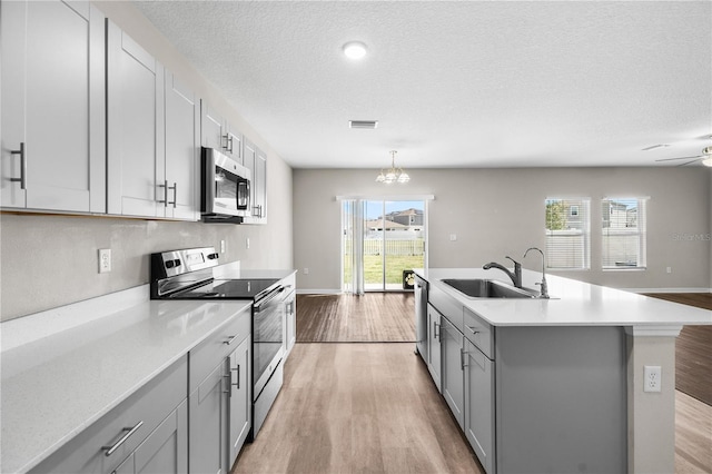 kitchen with stainless steel appliances, gray cabinets, light countertops, light wood-style floors, and a sink