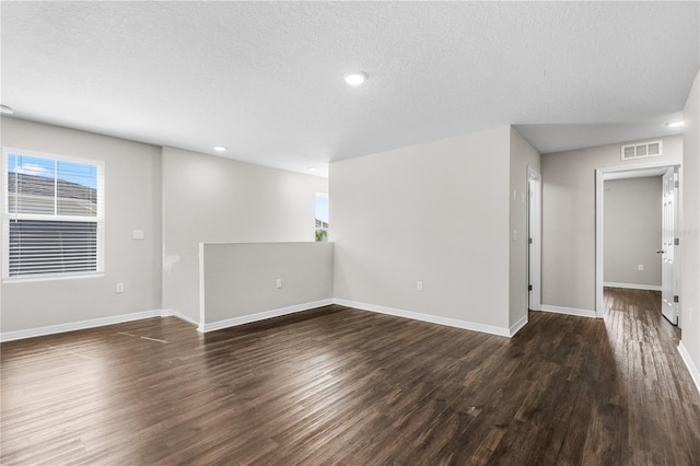 empty room with a textured ceiling, recessed lighting, wood finished floors, visible vents, and baseboards