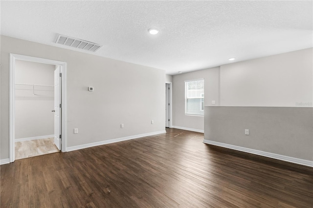 empty room featuring a textured ceiling, wood finished floors, visible vents, and baseboards