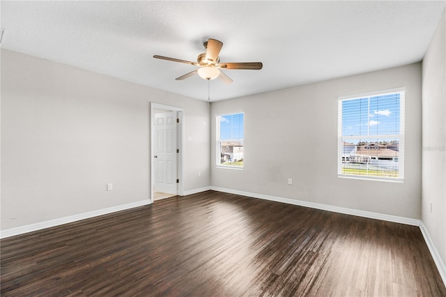 empty room featuring dark wood-style floors, plenty of natural light, baseboards, and a ceiling fan