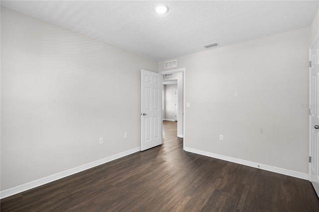 spare room featuring dark wood-style floors, visible vents, and baseboards