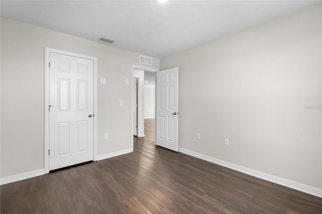 unfurnished bedroom with dark wood-type flooring, visible vents, and baseboards