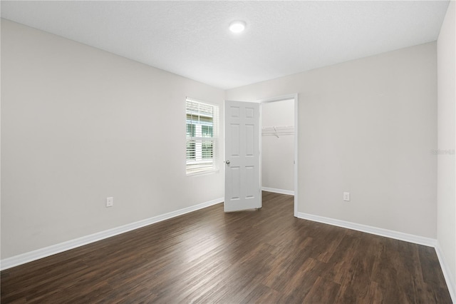 empty room featuring a textured ceiling, dark wood-type flooring, and baseboards