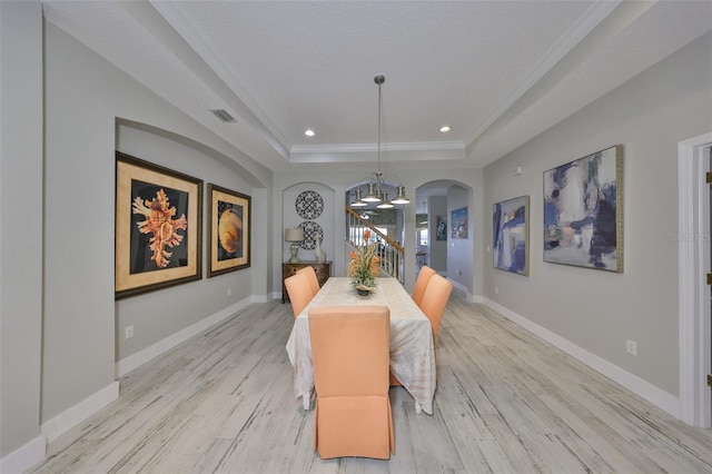 dining area with baseboards, arched walkways, a raised ceiling, light wood-type flooring, and a chandelier