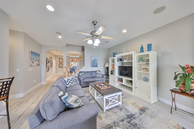 living room featuring arched walkways, stairs, light wood-style flooring, and recessed lighting