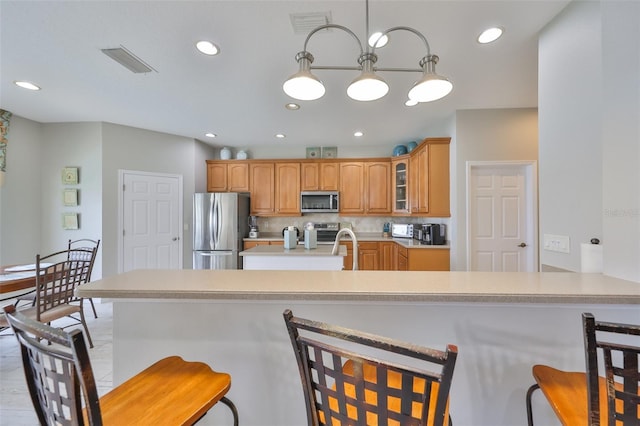 kitchen with visible vents, glass insert cabinets, stainless steel appliances, light countertops, and a kitchen bar