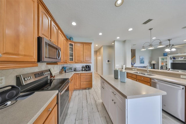 kitchen featuring stainless steel appliances, light countertops, glass insert cabinets, white cabinets, and a sink