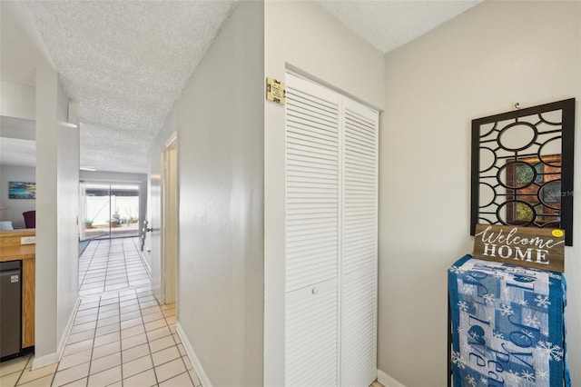 corridor with baseboards, a textured ceiling, and light tile patterned flooring