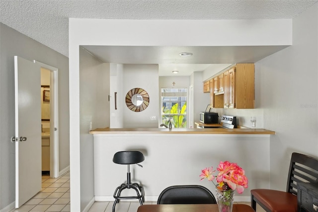 kitchen featuring light tile patterned flooring, a textured ceiling, a kitchen breakfast bar, a peninsula, and baseboards