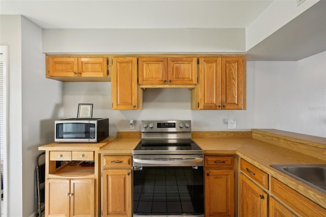 kitchen with a sink, brown cabinetry, stainless steel appliances, and light countertops