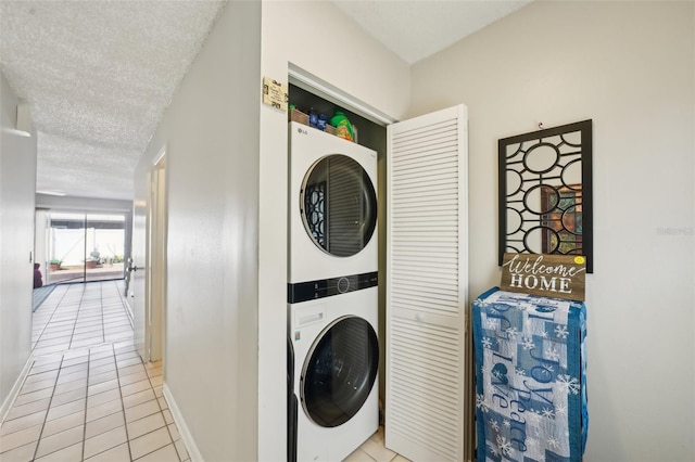 washroom featuring stacked washer and clothes dryer, light tile patterned floors, a textured ceiling, laundry area, and baseboards