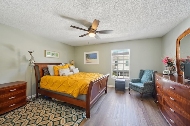 bedroom with ceiling fan, a textured ceiling, baseboards, and wood finished floors