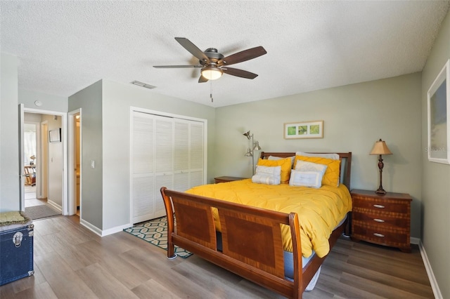 bedroom featuring baseboards, visible vents, wood finished floors, a textured ceiling, and a closet