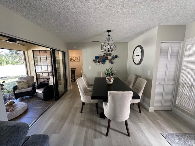 dining space featuring a notable chandelier, light wood finished floors, visible vents, a textured ceiling, and baseboards