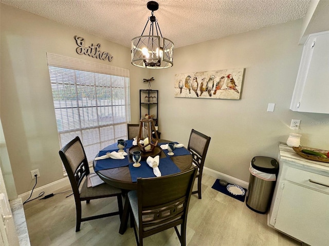 dining area with a textured ceiling, light wood-type flooring, an inviting chandelier, and baseboards