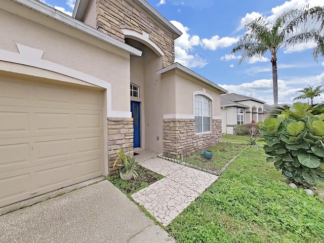 property entrance with stone siding, a yard, an attached garage, and stucco siding