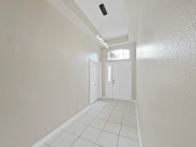 entrance foyer with light tile patterned floors, a raised ceiling, and baseboards