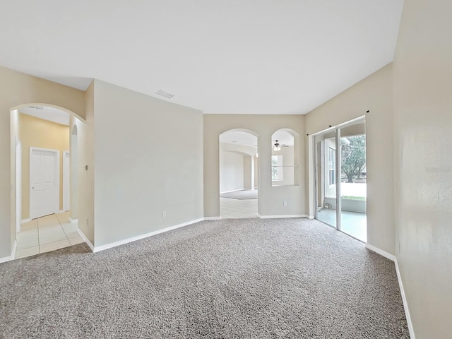 spare room with carpet, visible vents, arched walkways, and baseboards