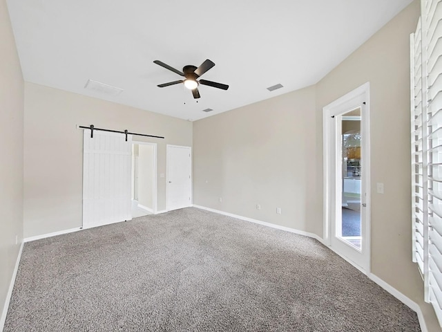 unfurnished bedroom with carpet floors, a barn door, and baseboards