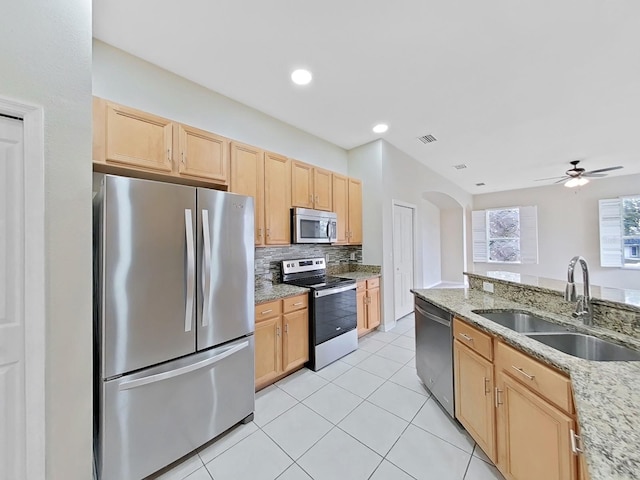 kitchen featuring arched walkways, light tile patterned floors, light brown cabinets, a sink, and appliances with stainless steel finishes