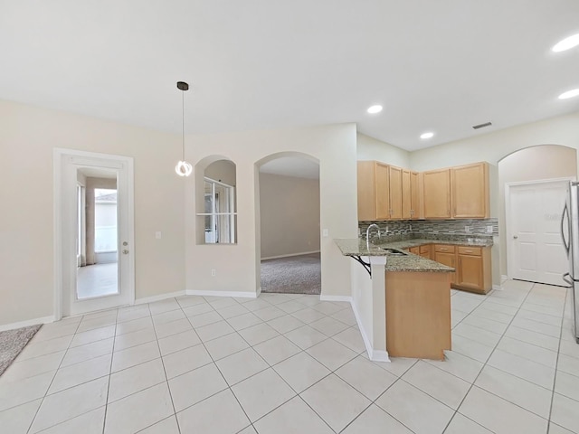 kitchen featuring a peninsula, stone counters, light tile patterned floors, and decorative backsplash