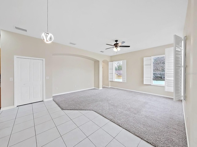 spare room featuring arched walkways, light tile patterned floors, visible vents, a ceiling fan, and light carpet